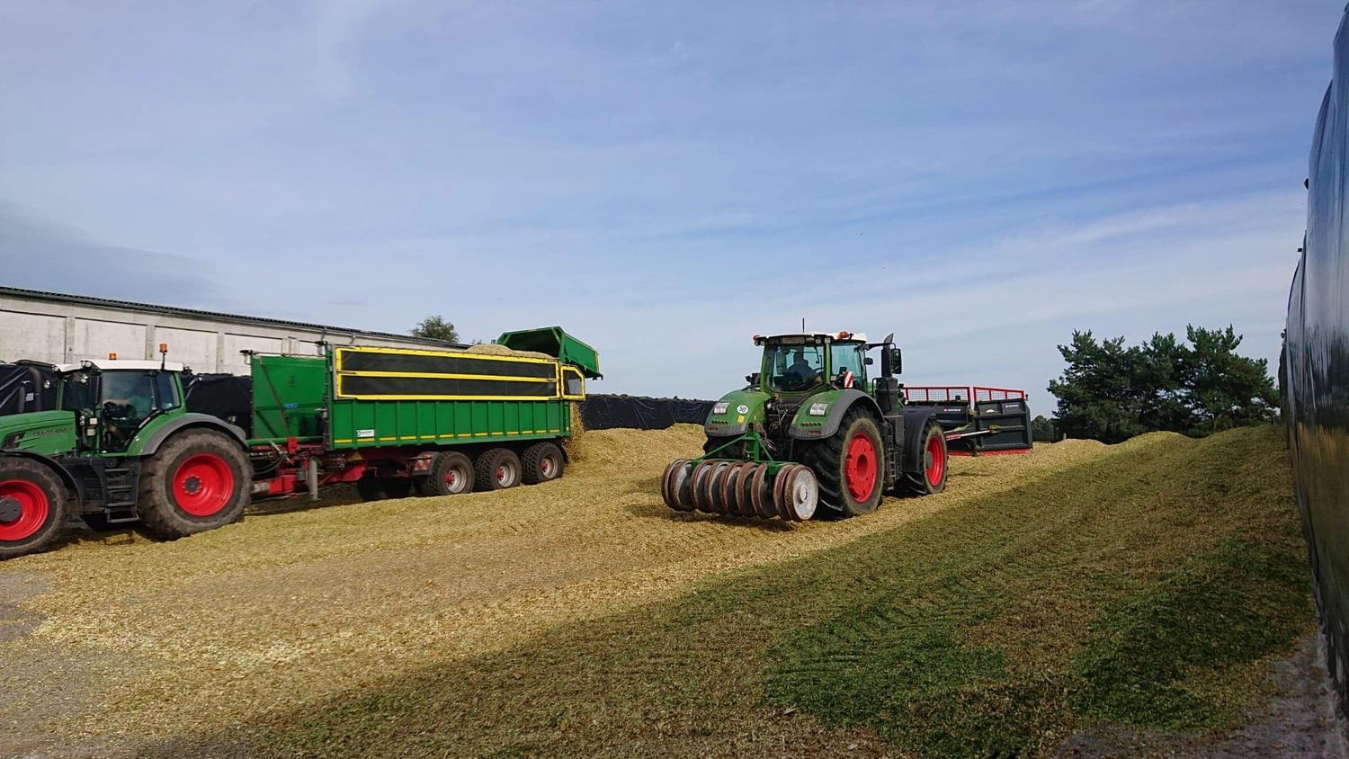 Agrargemeinschaft Holthusen e.G. - Landwirtschaftlicher - In der Mitte ein grüner Fendt-Traktor, der anscheinend mit einer Walze zum Verdichten von Silage auf einem Bauernhof ausgestattet ist.